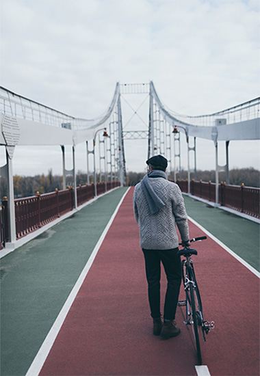 Rear view of a man pushing a bicycle on a bridge